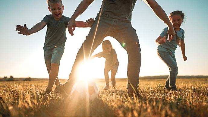 Familj som spelar fotboll på en äng